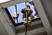 A Marine sits at the opening of a square hole holding a rope between his arms and legs.