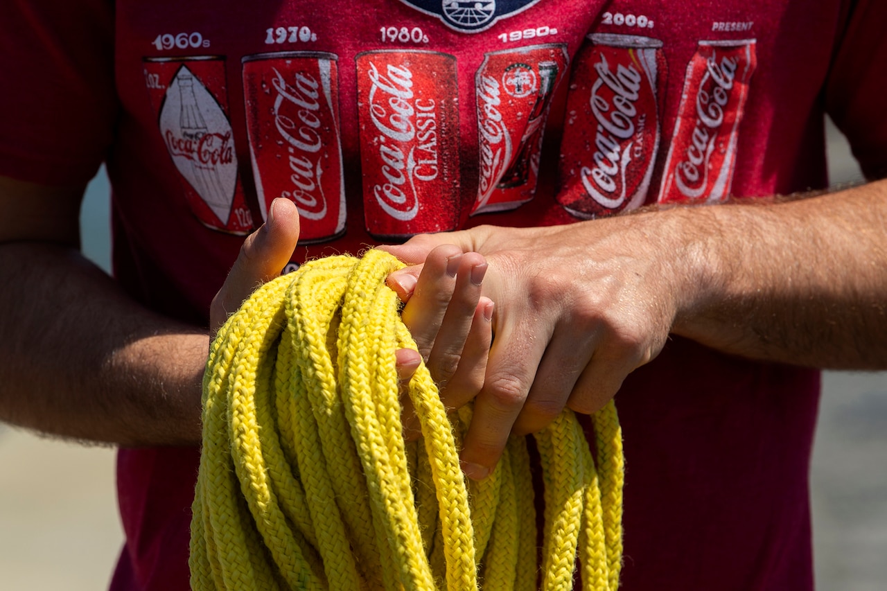 A man in a red T-shirt coils rope.