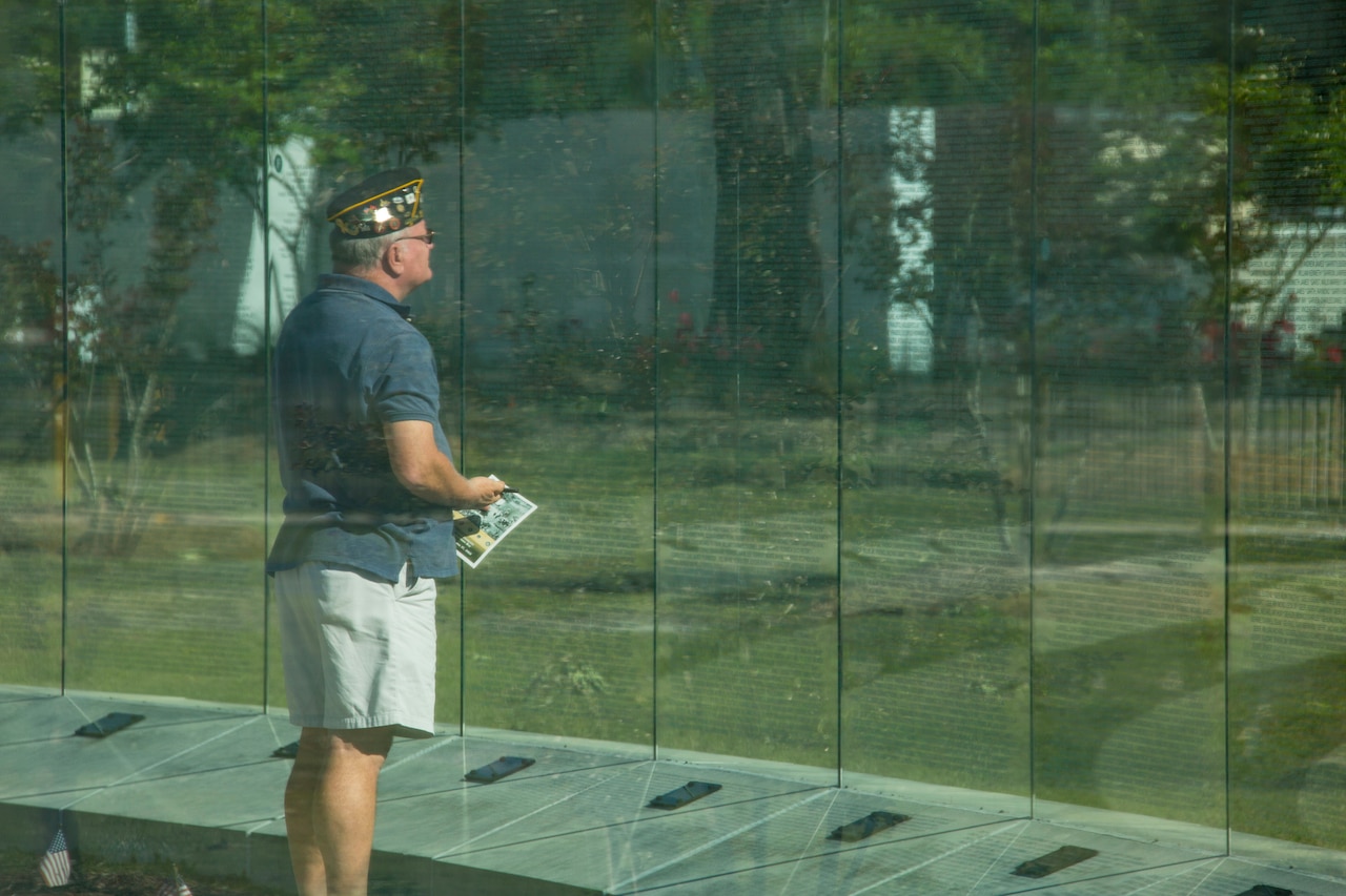 Man reads names on glass wall.