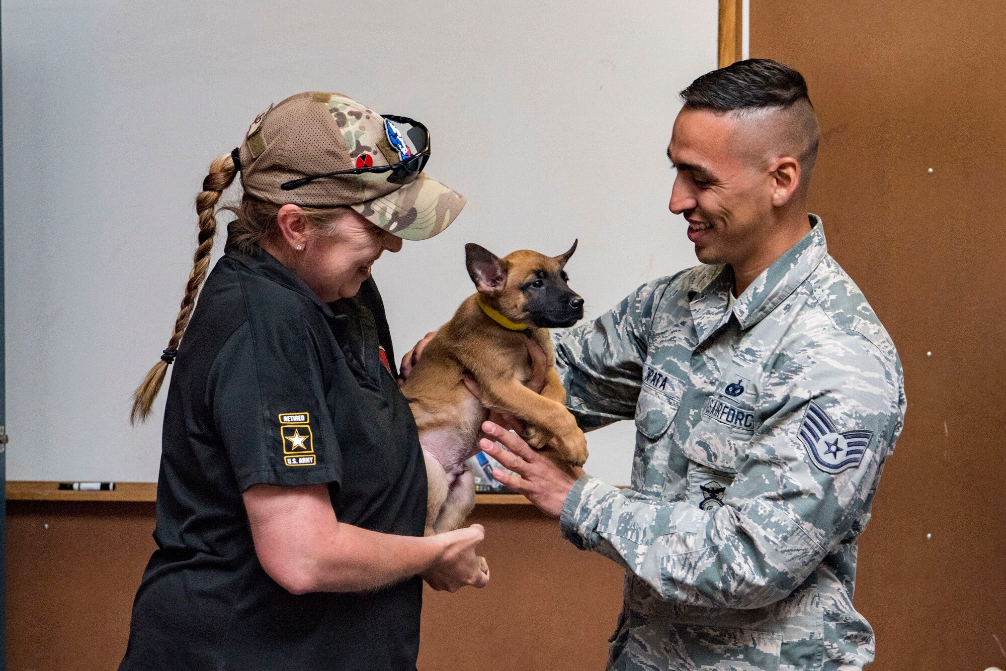 Regina Johnson, 341st Training Wing MWD breeding program foster consultant, hands a military working dog puppy to Staff Sgt. Carlos Zapata, 341st Training Squadron logistics NCO, April 26, 2019, at Joint Base San Antonio-Lackland, Texas. The Joint Base San Antonio military working dog foster puppy program places fosters with four-legged future warriors for six months before they enter the next phase of specialized training.