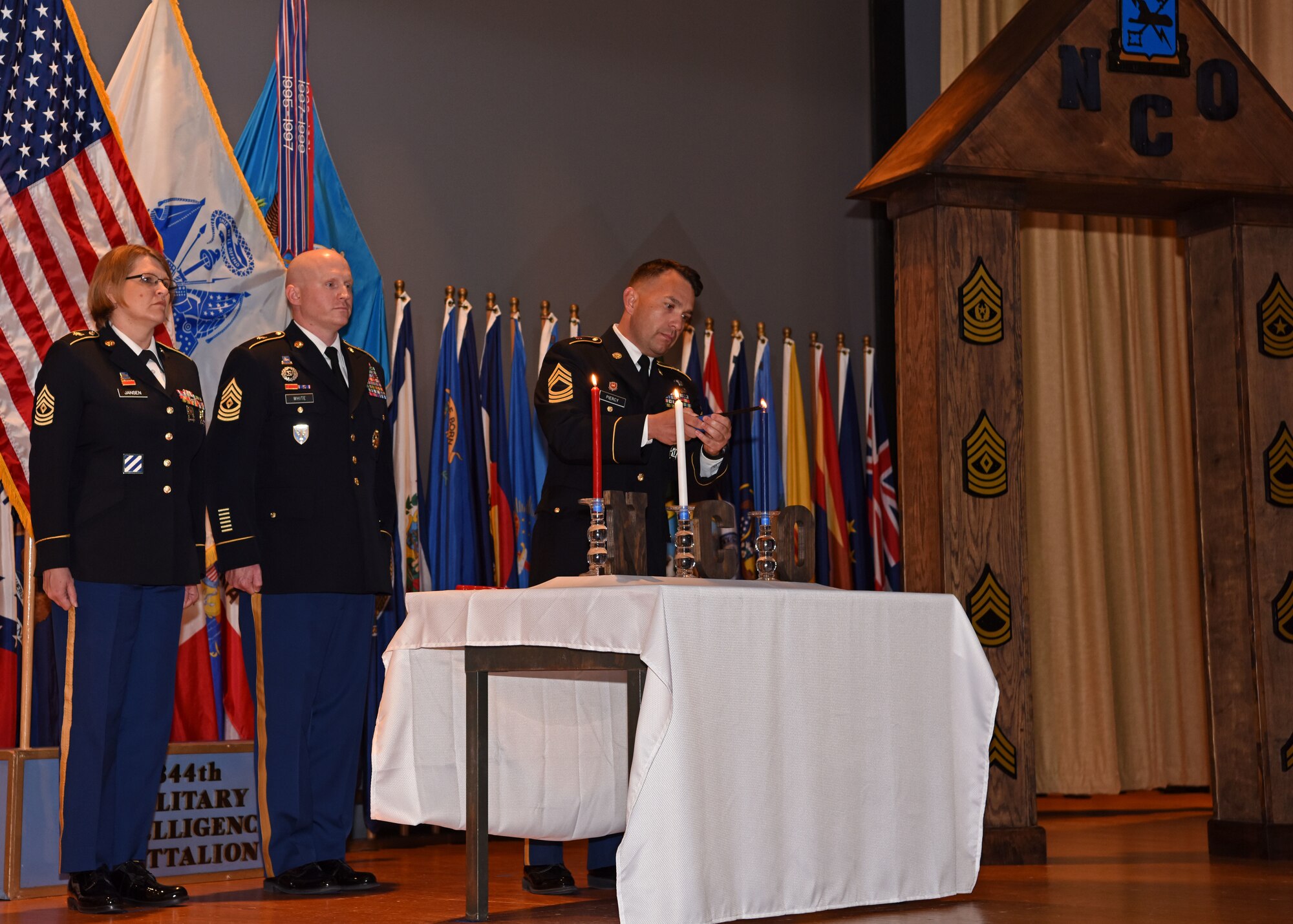 U.S. Army Master Sgt. Lorie Jansen, Master Sgt. Brandon White, and Master Sgt. Jason Piercy, members of the 344th Military Intelligence Battalion, light the candles at the Noncommissioned Officer Induction Ceremony at the base theater on Goodfellow Air Force Base, May 21, 2019. The candles symbolize the blood of soldiers who died for the country, the purity of the NCO, and the future of the NCO. (U.S. Air Force photo by Airman 1st Class Ethan Sherwood/Released)