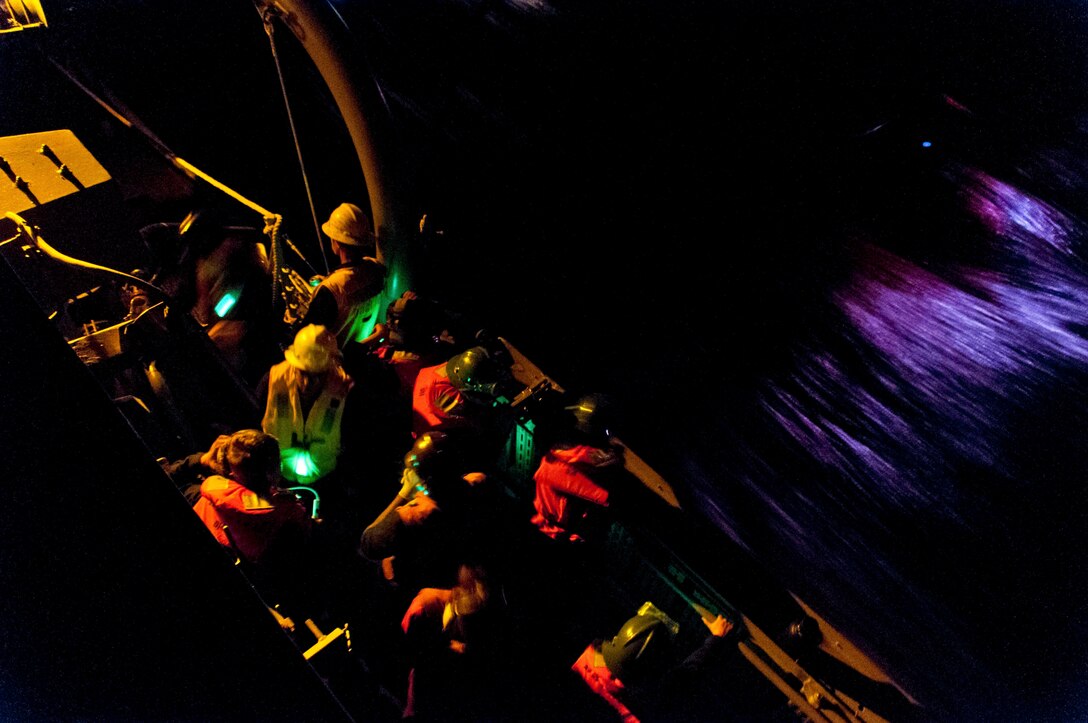 Sailors in multiple colors man a craft on the ocean at night.