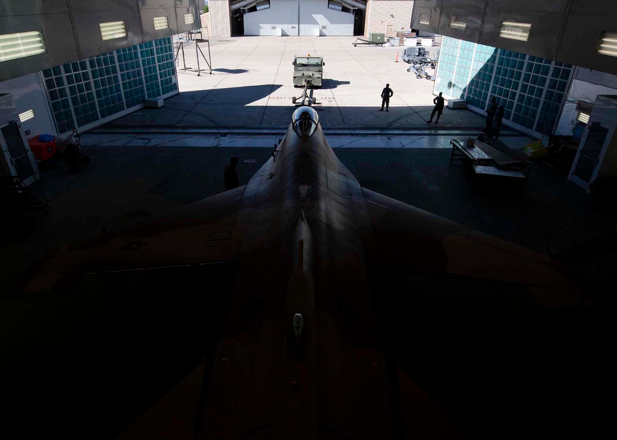 Airmen stand around and F-16 Fighting Falcon fighter jet as it gets towed into a corrosion shop.