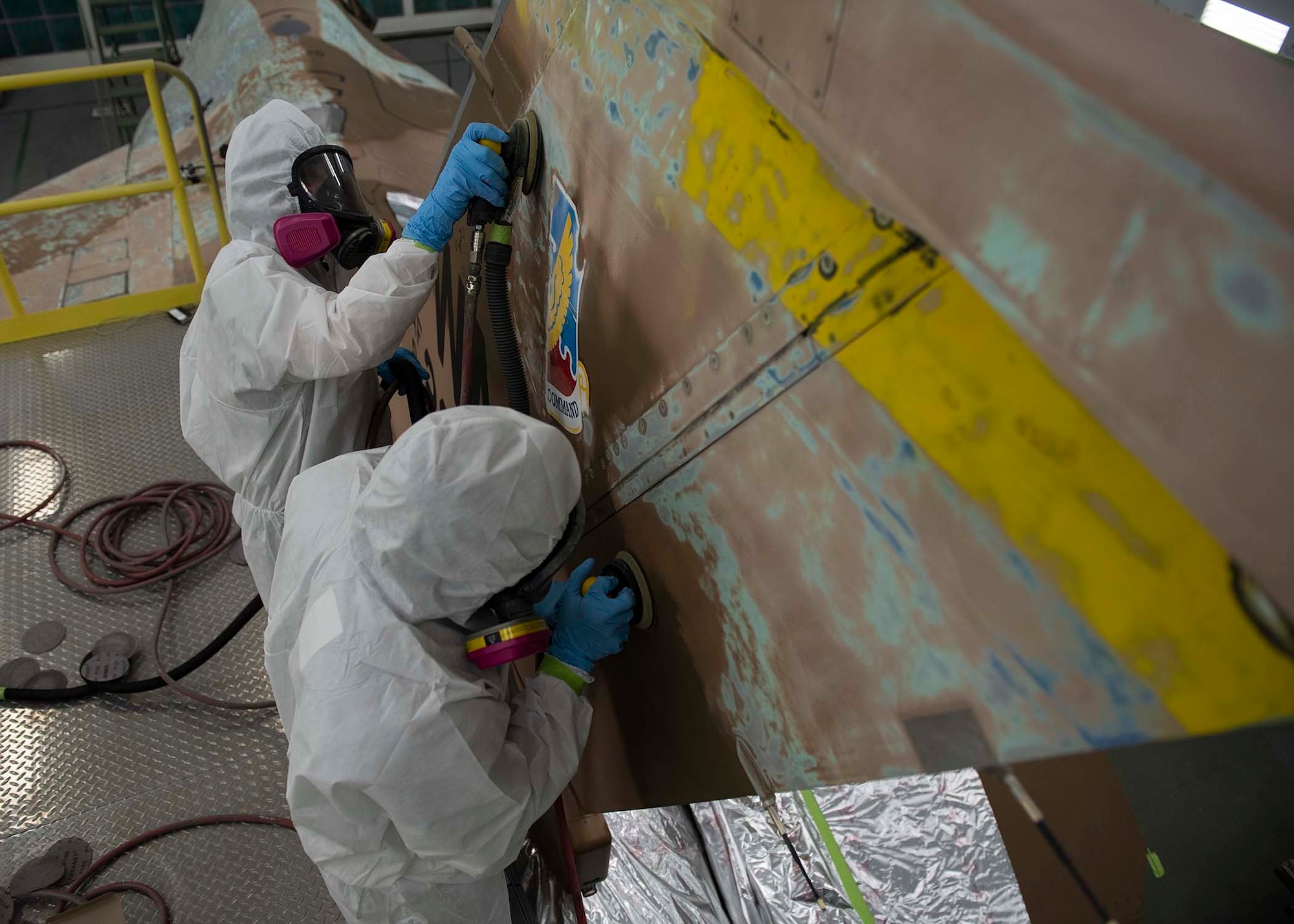 Two civilians sand the tail of an F-16 Fighting Falcon fighter jet.