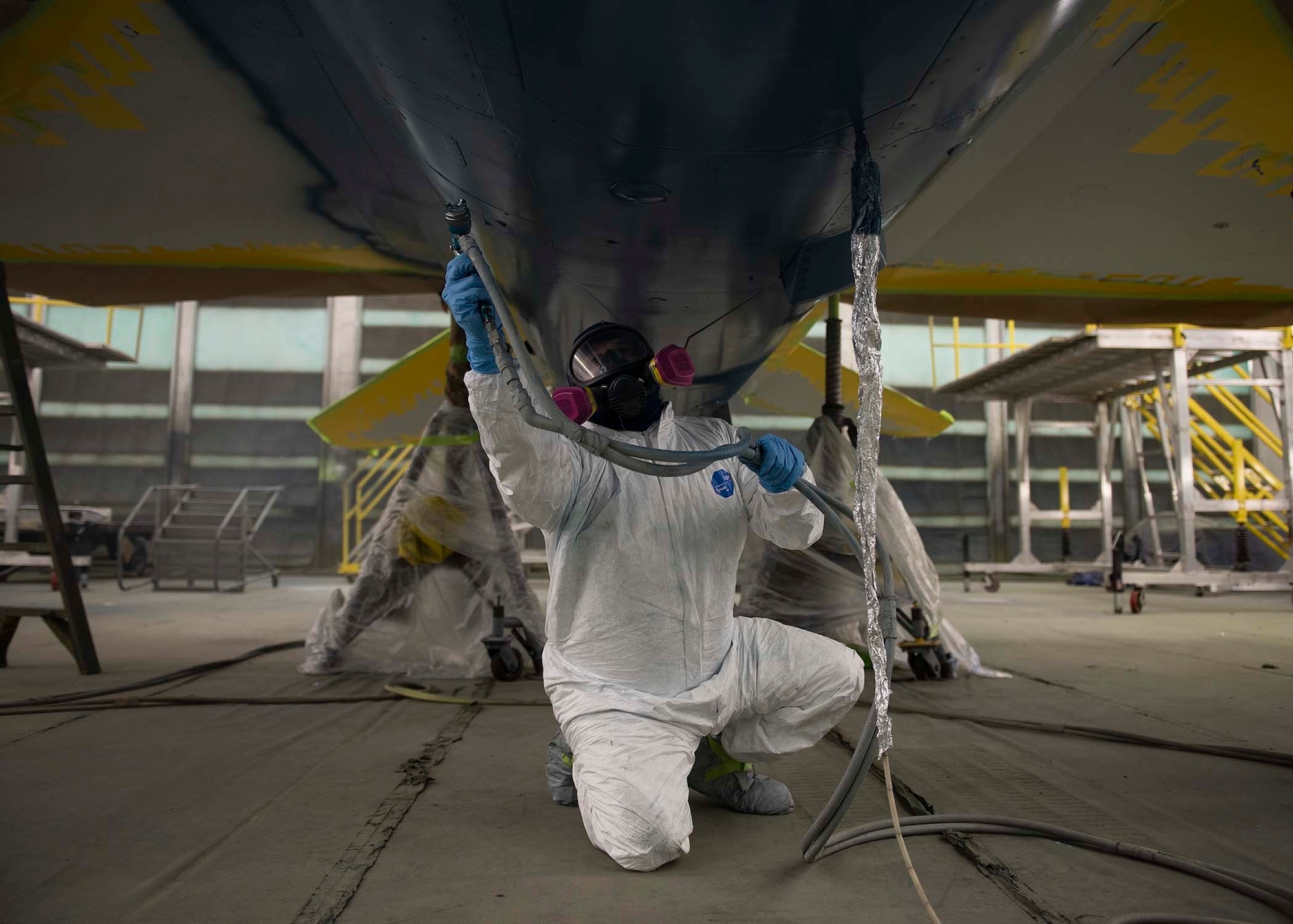 A civilian sprays paint on the bottom of a F-16 Fighting Falcon fighter jet.