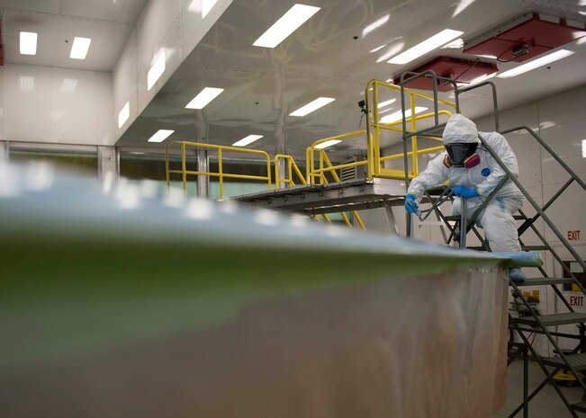 A civilian sprays paint onto the wing of an F-16 Fighting Falcon fighter jet