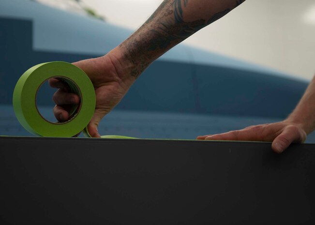 A civilian places tape on  an F-16 Fighting Falcon fighter jet.