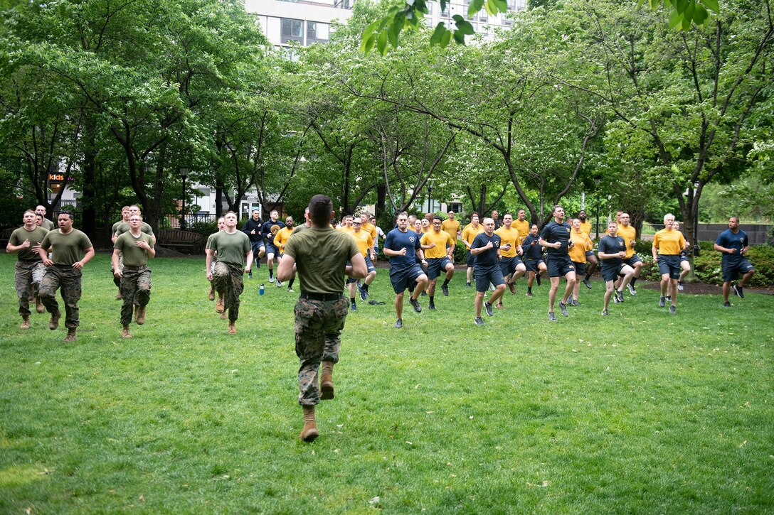 A group of marines and sailors run in place in a park.