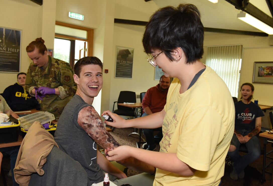 Amiko Groder, a volunteer, creates a mock wound on Garrett Evett, a simulated casualty, during a preparedness exercise at RAF Alconbury, England, May 20, 2019. The exercise tested the 501st Combat Support Wing preparedness and response capabilities to an emergency situation. (U.S. Air Force photo by Airman 1st Class Jennifer Zima)