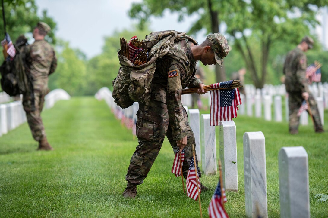 A soldier carries mini American flags at a cemetery.