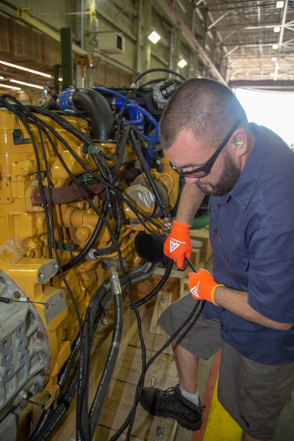 Jeremy Zubiate, Heavy Equipment Mechanic, attaches cables to a Medium Tactical Vehicle Replacement’s engine at Production Plant Barstow, Marine Depot Maintenance Command, on the Yermo Annex aboard Marine Corps Logistics Base Barstow, Calif., May 7.