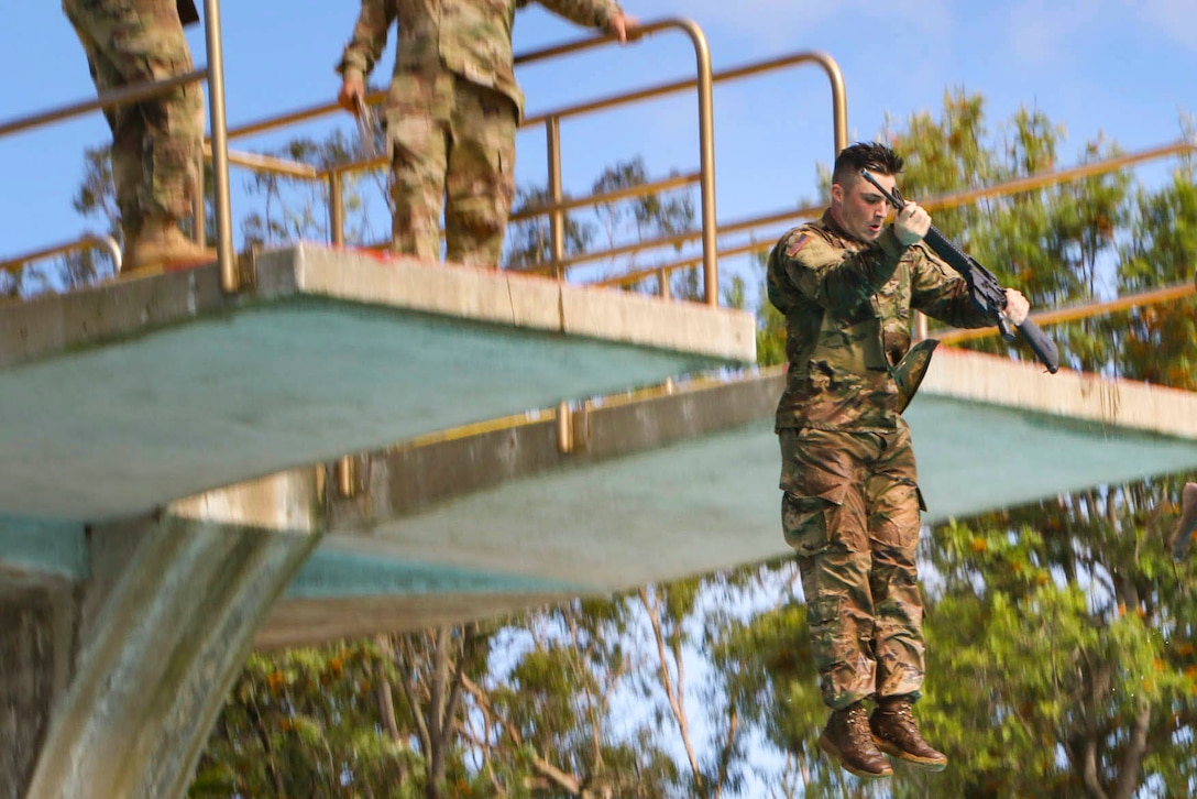 A soldier jumps off a high dive holding a rubber gun.