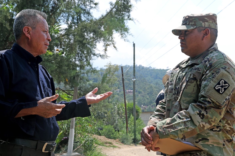 A man and a soldier converse outdoors.