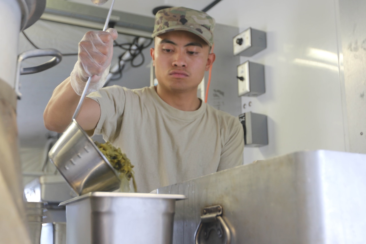 A soldier uses a ladle to put food into a pan.