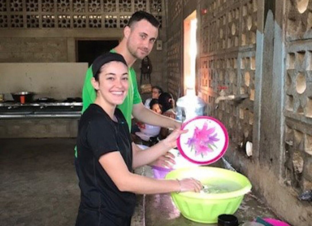 Man and woman wash dishes in a plastic bucket.