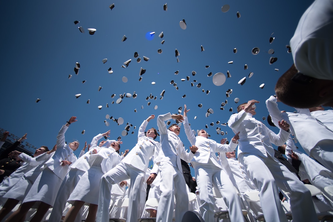 A group of graduating sailors toss hats in the air.