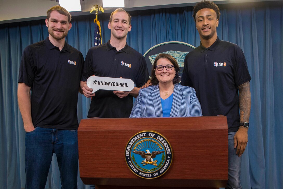 Kim Joiner, the acting principal deputy assistant to the secretary of defense for public affairs, stands at a podium with three men.