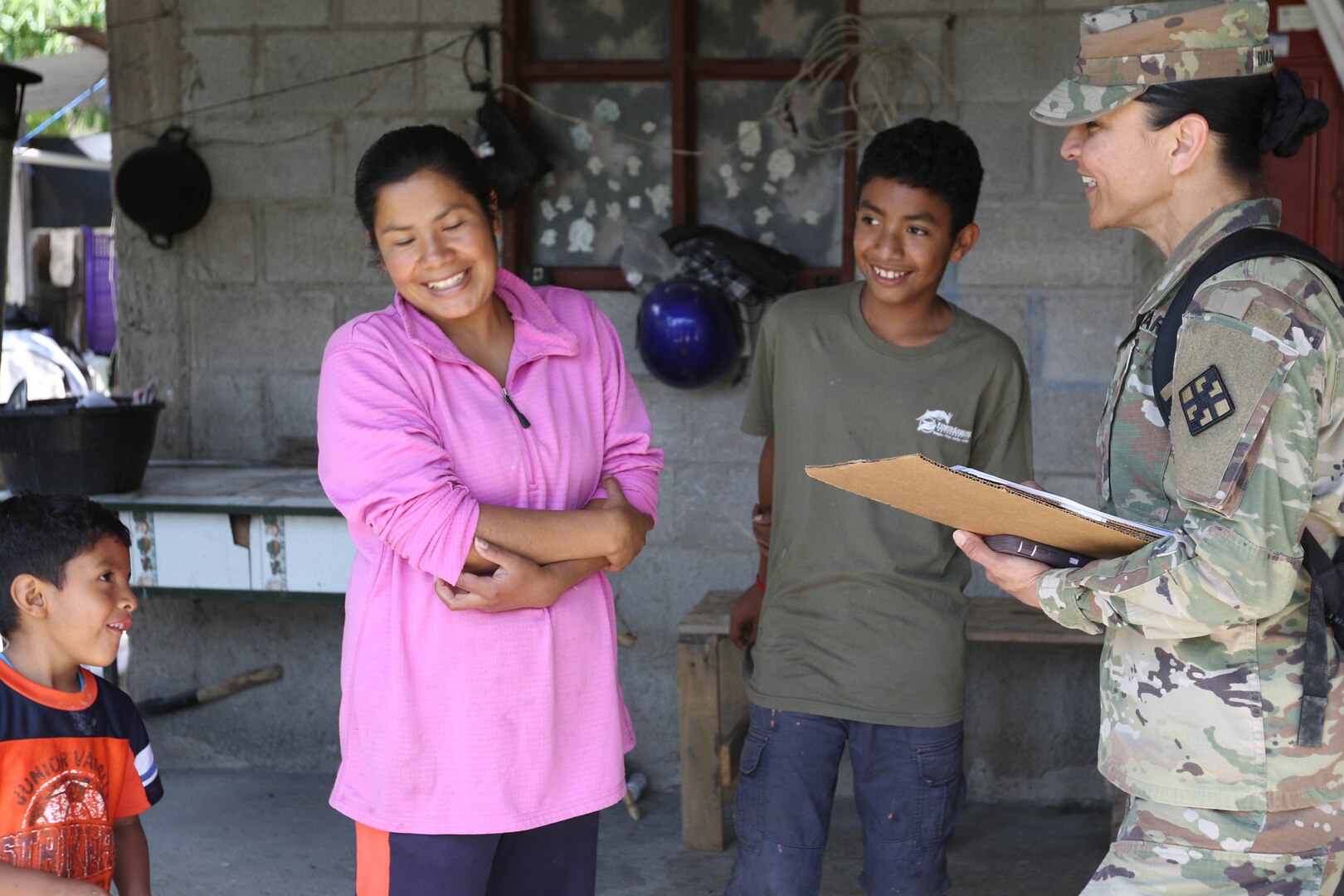 A soldier with a clipboard talks with a woman and her children.