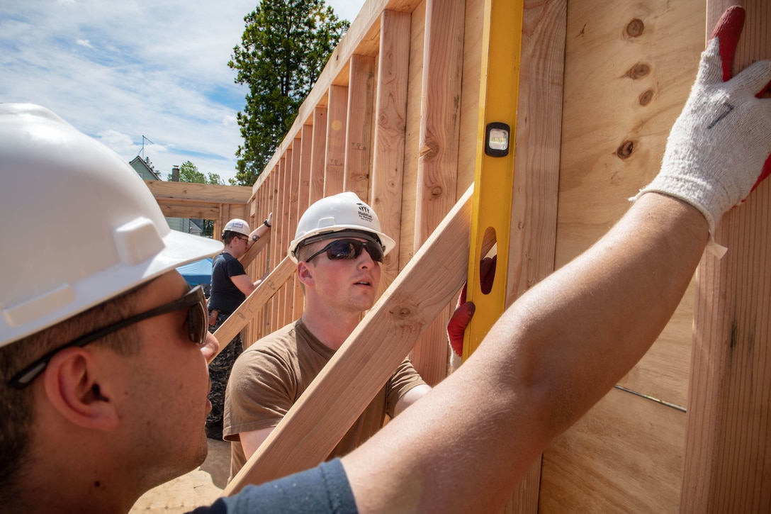 Two sailors work on the siding of a house under construction.