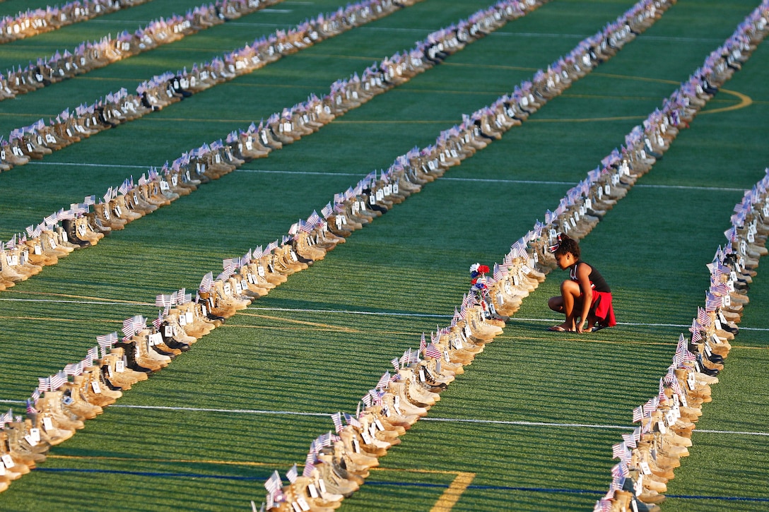 A young girl examines boots displayed in rows on a field.