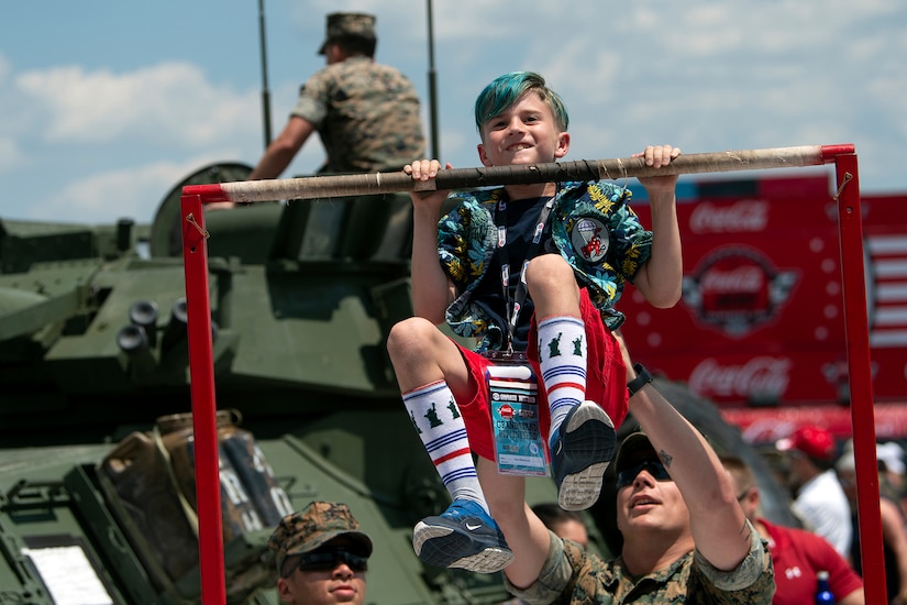 A boy does a pullup with the help of a service member.