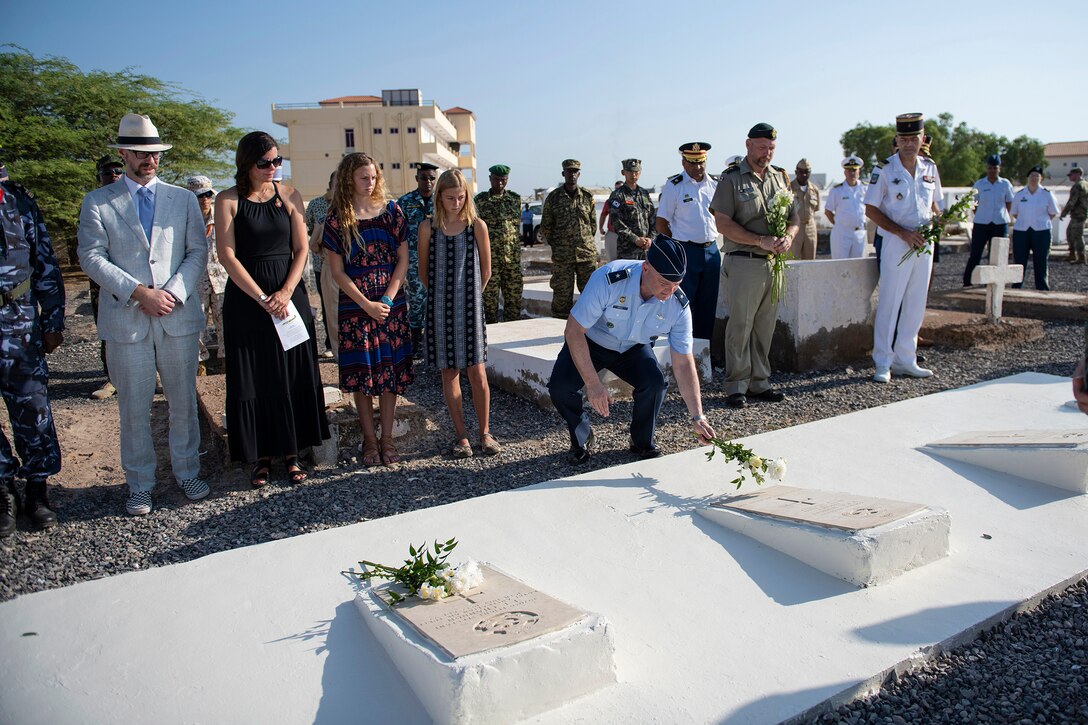 An airman surrounded by a group of people places flowers at a grave.