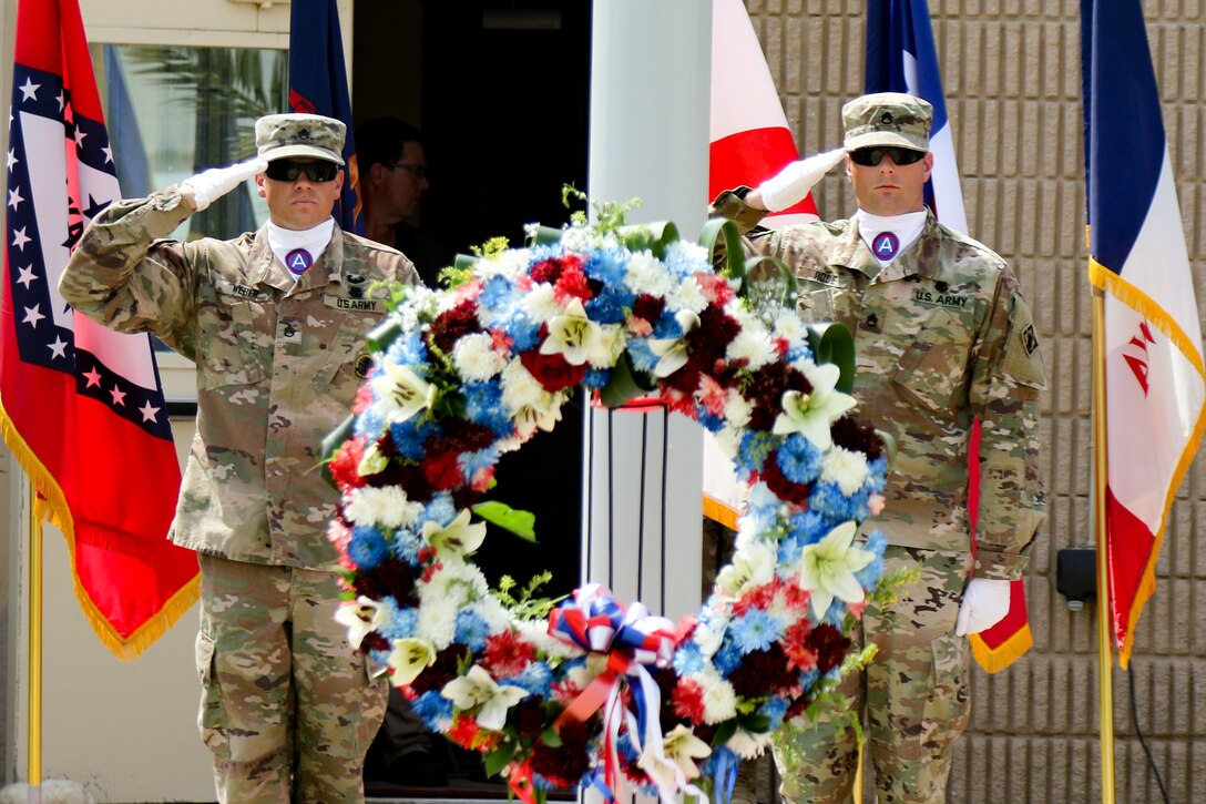 Two service members stand and salute on either side of a wreath.