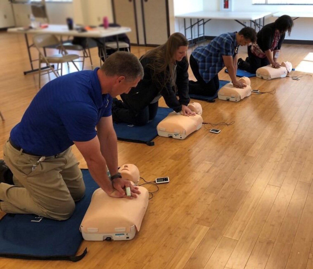 Four class members practice CPR compressions on training body.