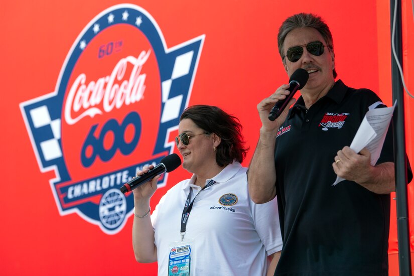 A man and a woman speak into microphones from a stage.