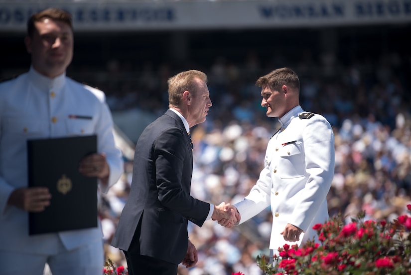 A man in a suit shakes hands with a man in uniform.