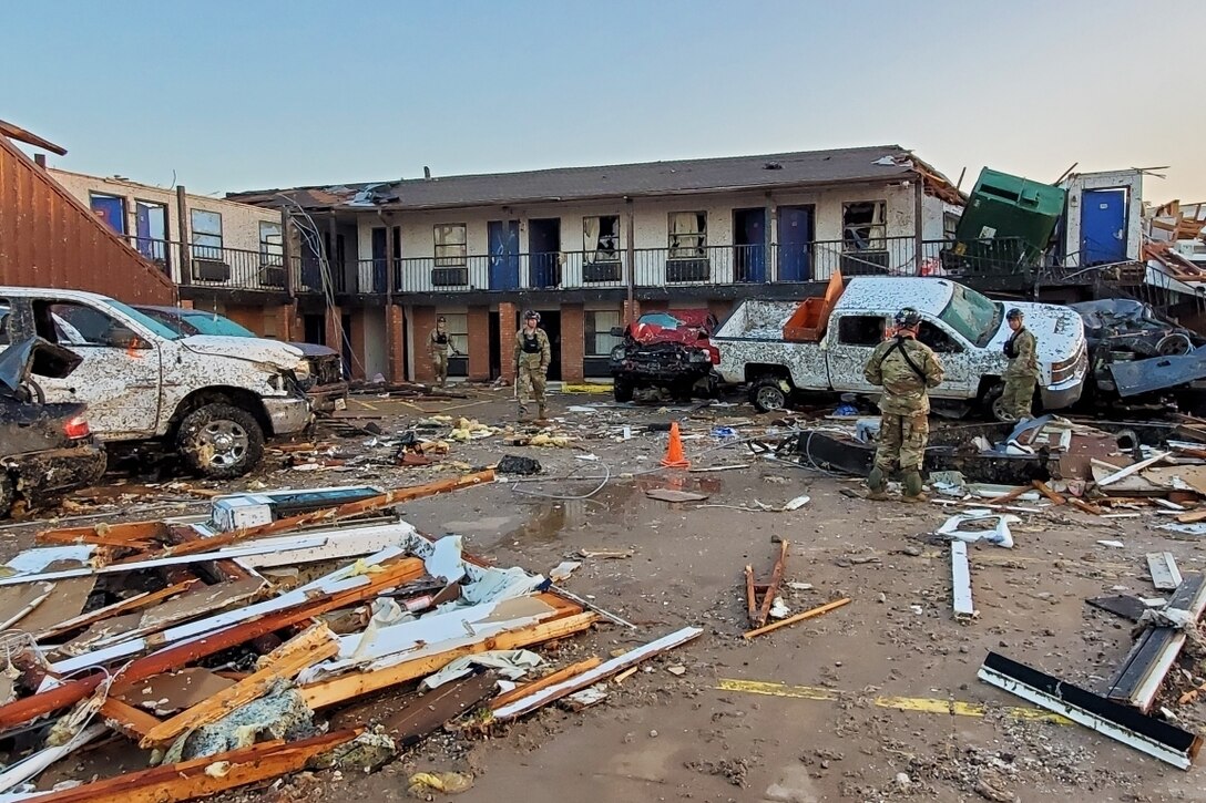 Service members walk among tornado debris in front of a motel.