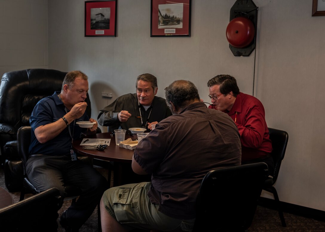 Four men sit at table with pen and paper taste testing chili