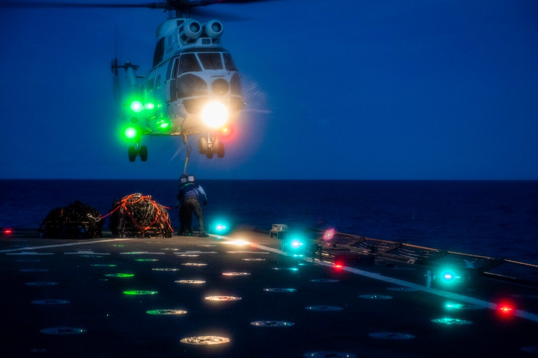 Sailors attach cargo to a helicopter at night.