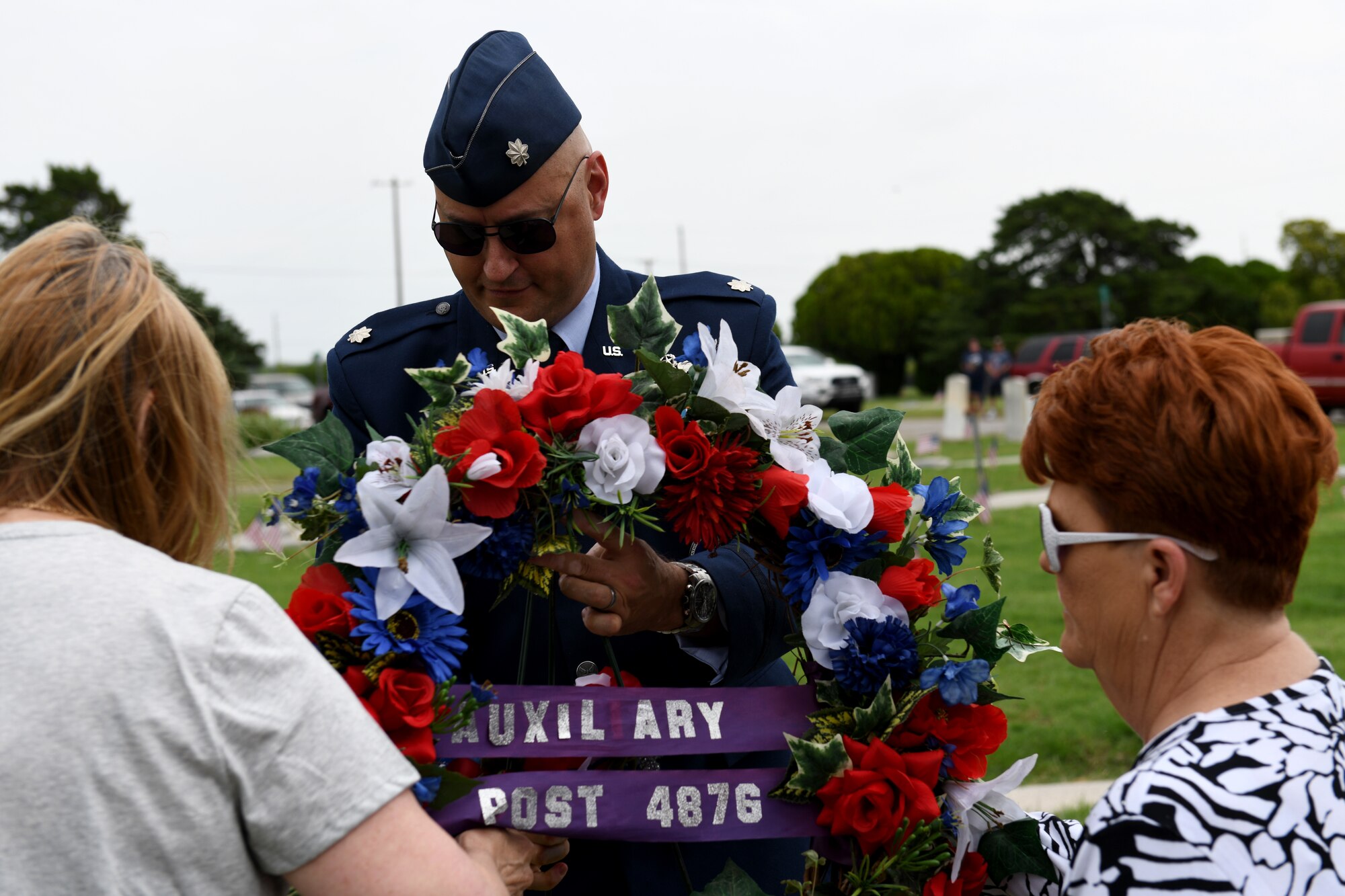Lt. Col. Justin Capper, commander of the 54th Air Refueling Squadron, picks up a wreath with several community members to place it before a memorial tombstone on Memorial Day, May 27, 2019, at Altus, Okla. This was part of a ceremony honoring fallen service members.