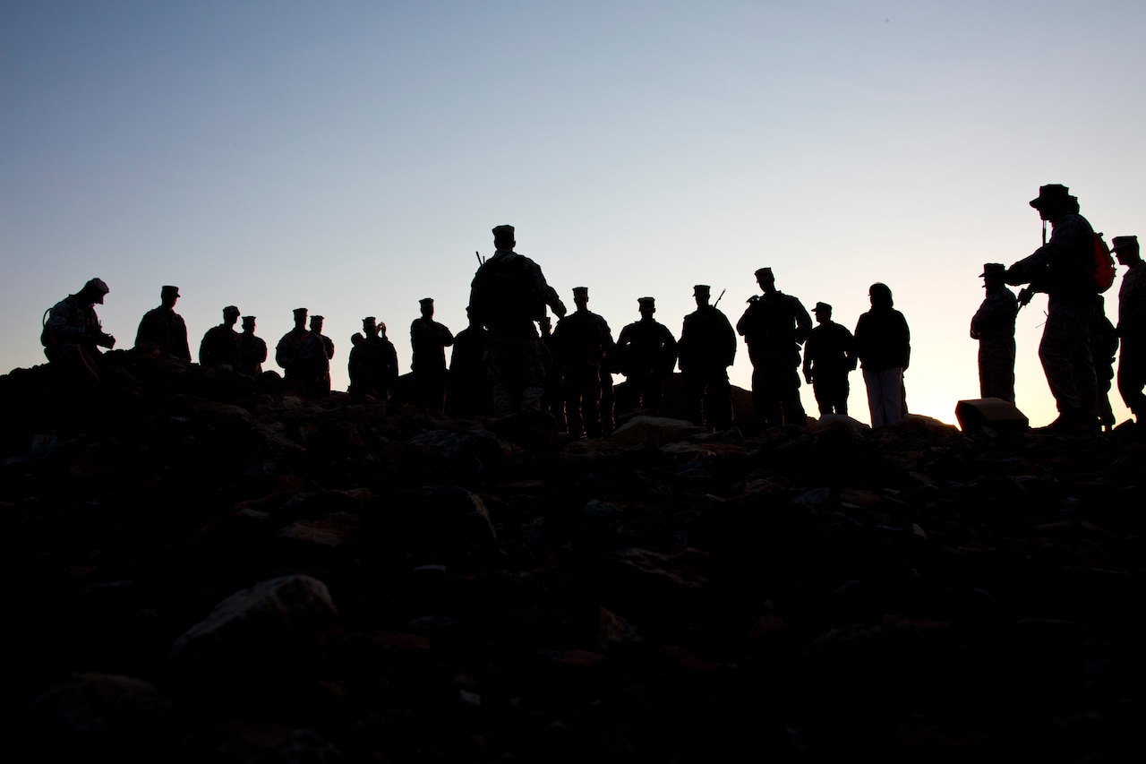 More than a dozen Marines in silhouette gather for a briefing.