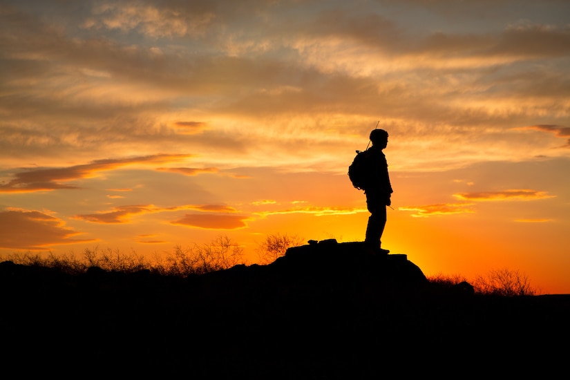 A lone soldier stands in silhouette on a hilltop.