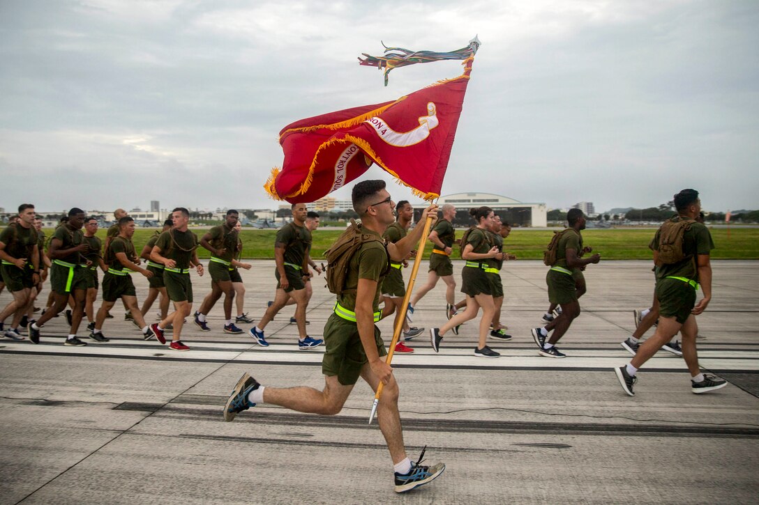 A Marine carrying a flag runs with a group of fellow Marines.