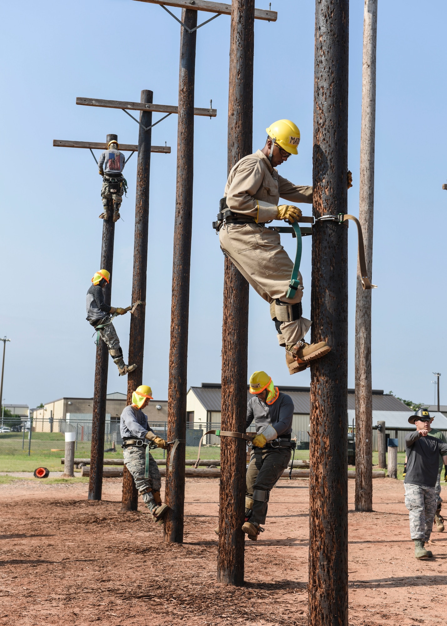 366th Training Squadron electrical systems apprentice course students climb up poles during training at Sheppard Air Force Base, Texas, May 28, 2019. Using a collection of straps, metal ridges and the super squeeze belt, the climbers are able to grip the pole and eliminates the danger and fear of slipping. (U.S. Air Force photo by Senior Airman Ilyana A. Escalona)