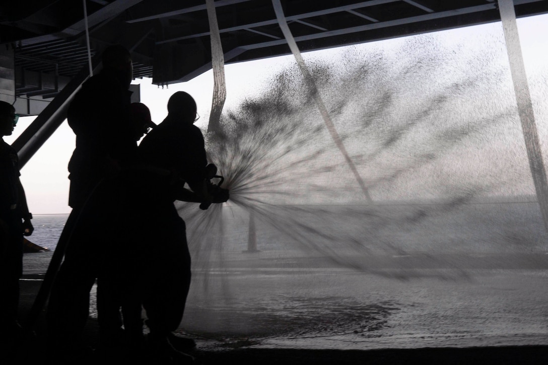 Sailors use a hose to spray the floor of a ship.