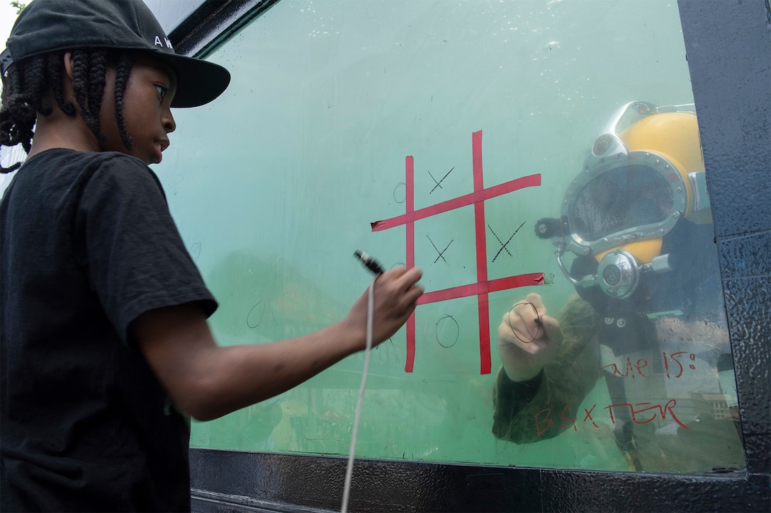 A sailor plays tic-tac-toe with a child.