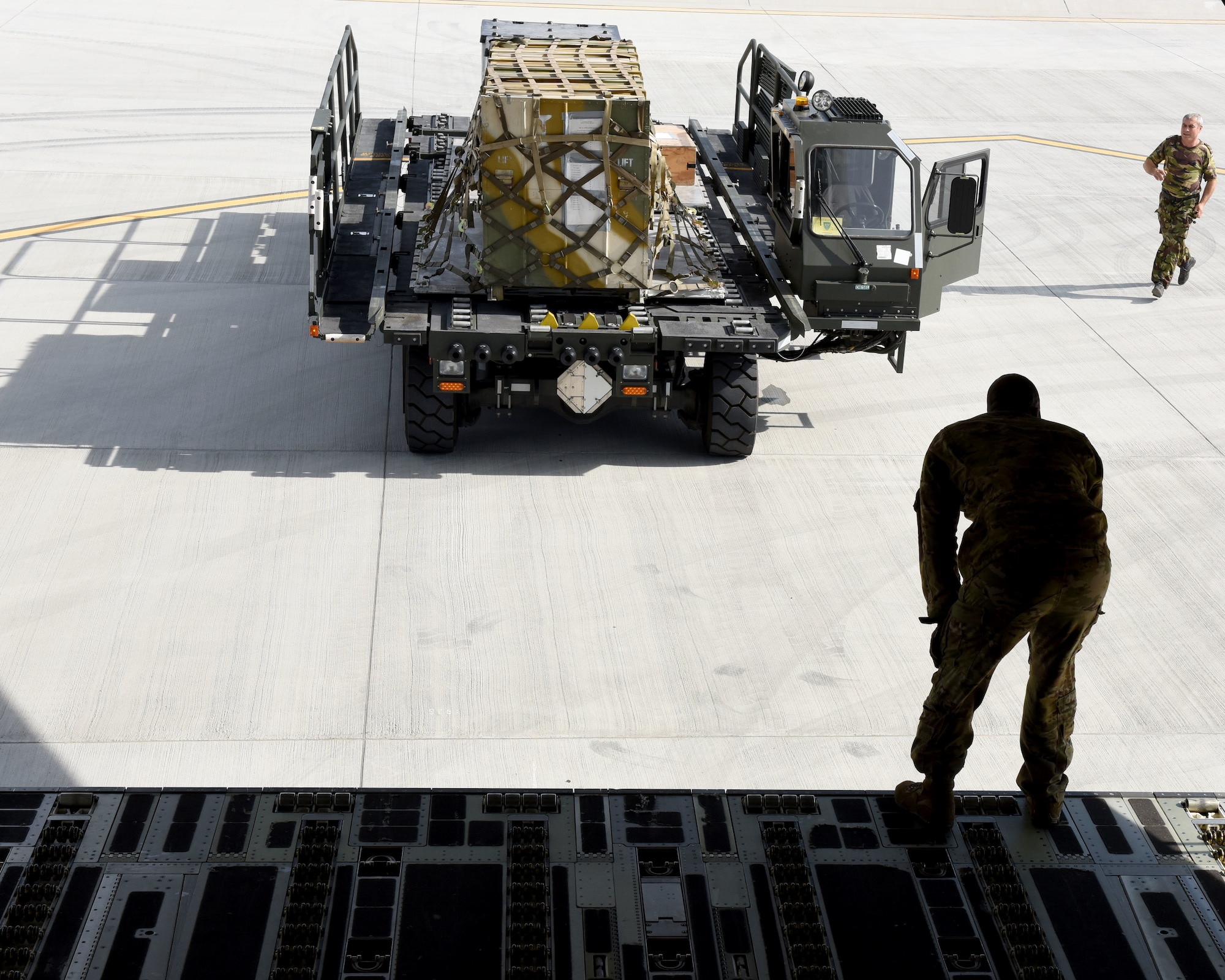 U.S. Air Force Staff Sgt. James Armstrong, 21st Airlift Squadron loadmaster, waits as a member of the Romanian armed forces runs to finish loading cargo and equipment onto a C-17 Globemaster III, May 25, 2019, in Bucharest, Romania. With more than 730 personnel deployed to Afghanistan, Romania is the sixth largest contributor of troops to NATO’s Resolute Support Mission. (U.S. Air Force photo by 2nd Lt. R. Michael Longoria)