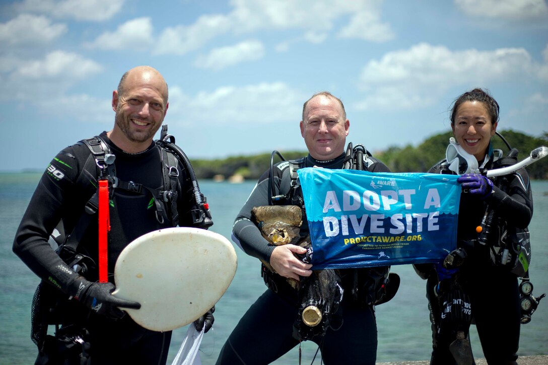 地元ダイバーと米軍のダイバーが海底で拾ったゴミを手に記念撮影にポーズ。日米のダイバーが北谷町にある砂辺ビーチで５月２６日、海中クリーンアップ活動を行いました。