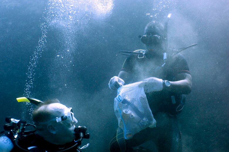 海底で拾った空き缶をゴミ袋に入れる海兵隊に所属する海軍衛生兵。地元ダイバーと米軍のダイバーが北谷町にある砂辺ビーチで５月２６日、海中クリーンアップ活動を行いました。