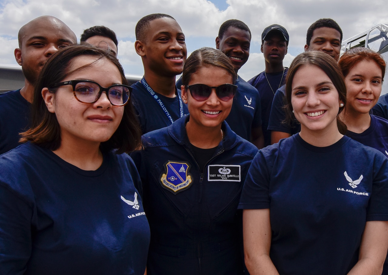 Nine Air Force recruits in blue Air Force T-shirts stand with an Air Force officer in a flight suit for a photo.