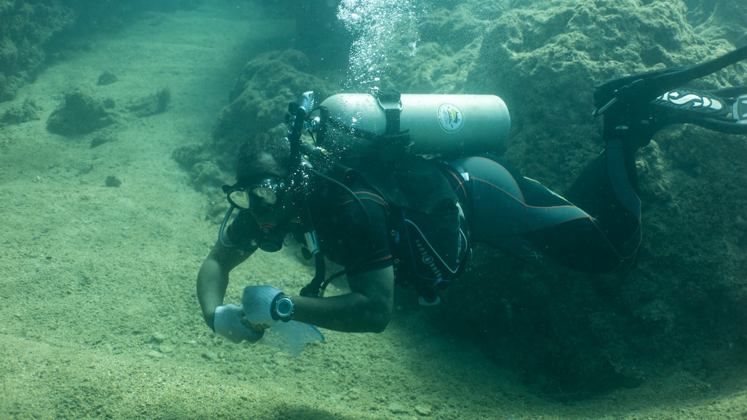 Petty Officer 2nd Class Alan Gooden, a hospital corpsman with 3rd Medical Battalion, 3rd Marine Logistics Group, tucks a can in a mesh bag during a scuba beach cleanup May 26, 2019 at Sunabe North Steps, Okinawa, Japan.