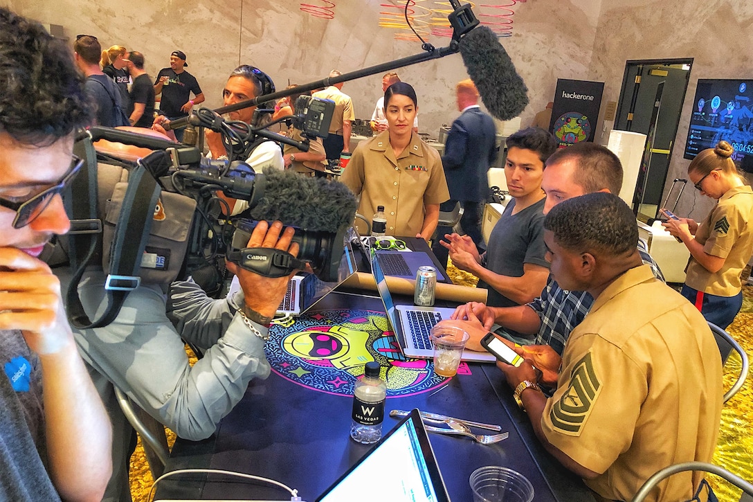 Marines and crowd around laptops in a small room.