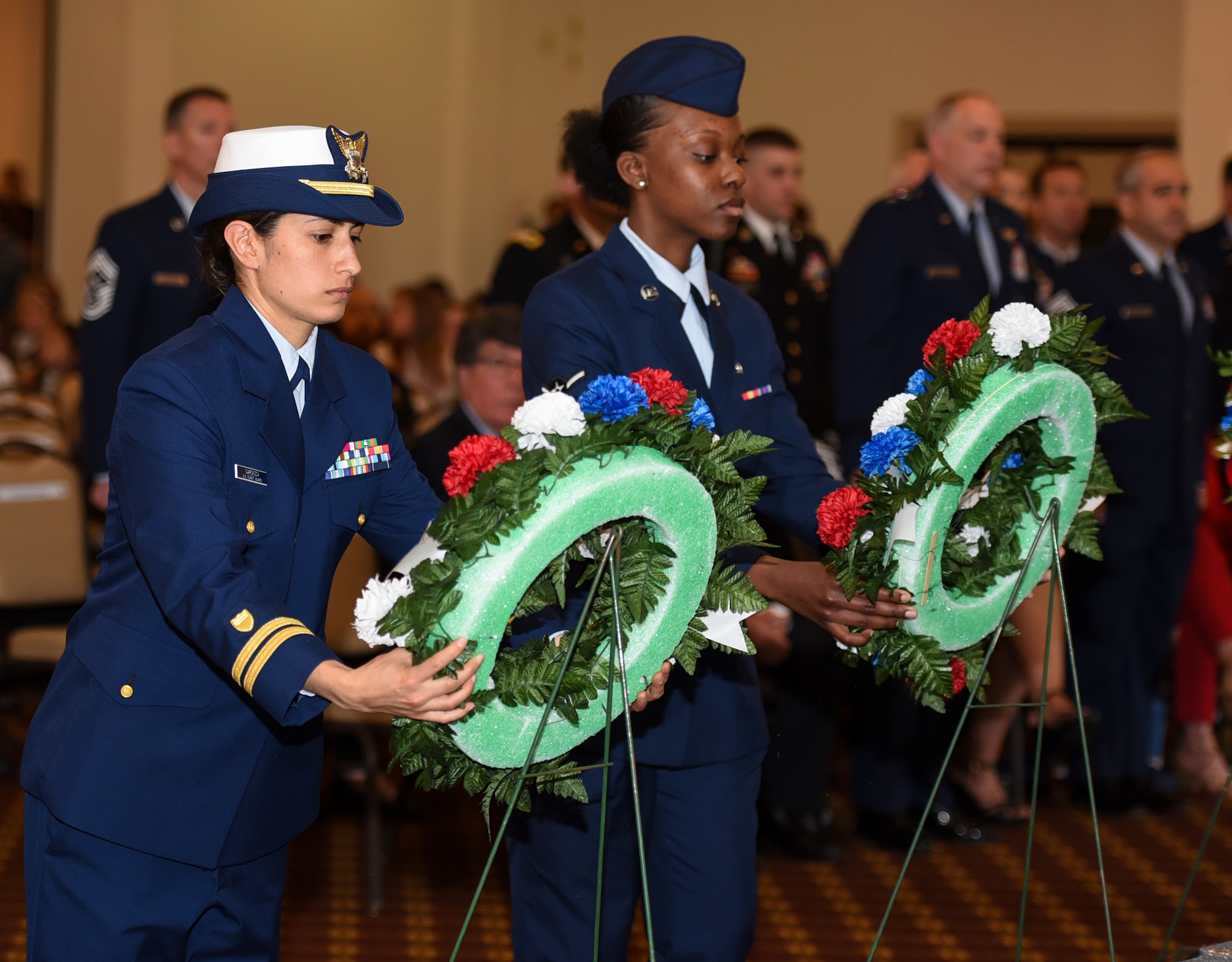 Lt. j.g. Samantha Cardoza, Atlantic Strike Team deck officer, and U.S. Air Force Airman Taneia Thomas, 87th Medical Group aerospace medical technician, hang wreaths representing their respective branch of service during the 37th Annual Parade of Wreaths on Joint Base McGuire-Dix-Lakehurst, New Jersey, May 23, 2019. This year, 13 service members have died fighting for our nation. Community members came together with their respective organizations to decorate a wreath and donate it to the ceremony presentation. (U.S. Air Force photo by Airman 1st Class Ariel Owings)