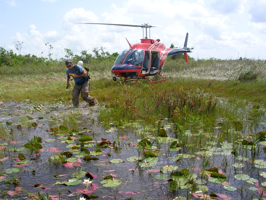 man in front of red helicopter walks into lake