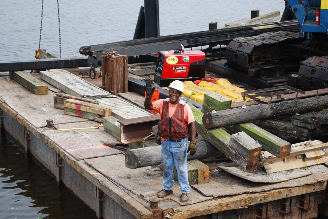 man standing in the dock with lots of wooden debris around him.