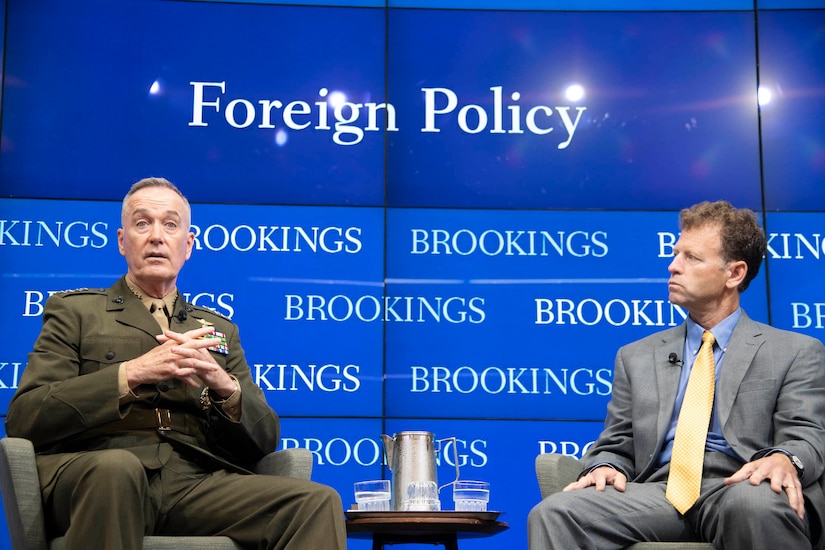 Marine general and civilian sit in chairs during a discussion panel.